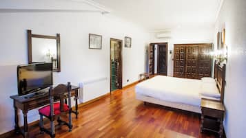 Un dormitorio con una cama, televisión sobre una mesa de madera, una silla y un armario.