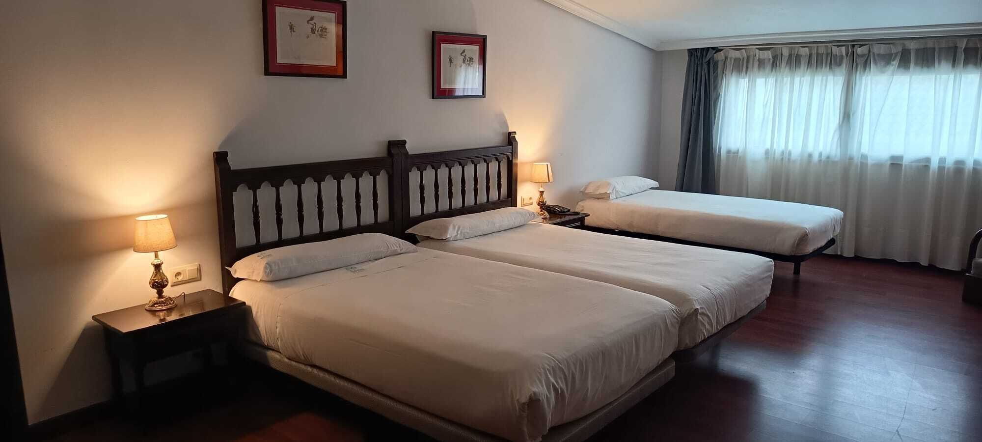Een hotelkamer met twee bedden, een nachtkastje met een lamp en een raam met gordijnen.