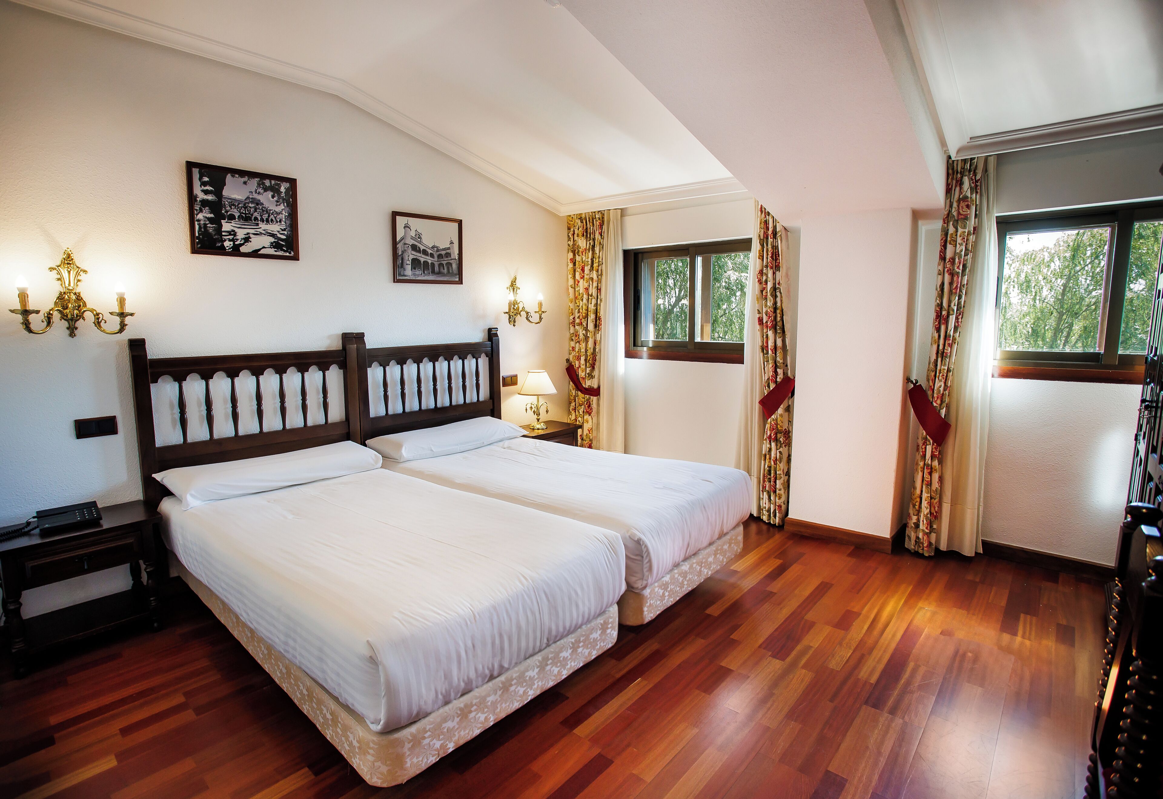 Ein Doppelbett mit Holz-Kopfteil, ein Nachttisch, zwei Wandleuchten und ein Fenster mit Vorhängen.