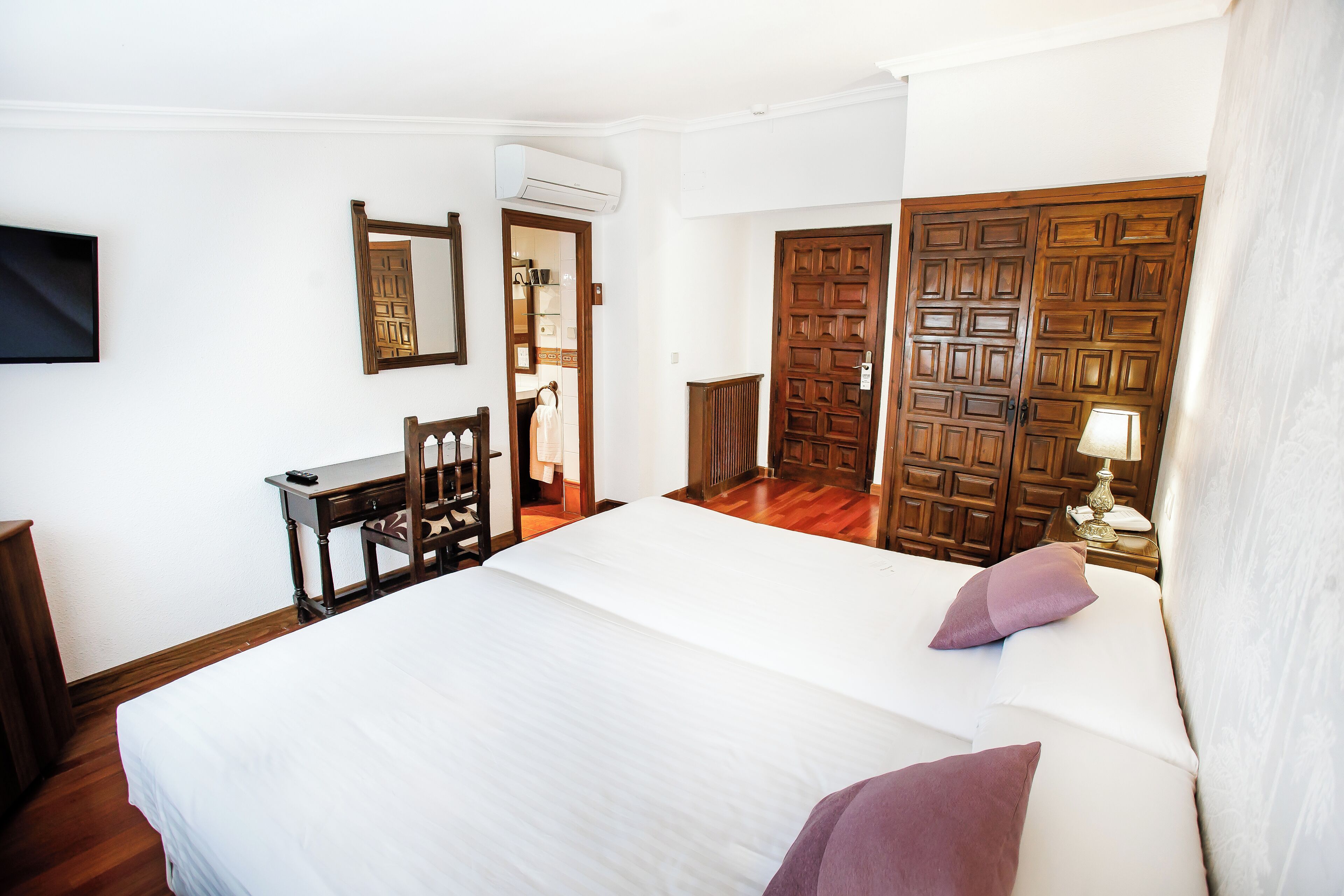 A hotel room with a large bed, wooden wardrobe, a desk, and a television.