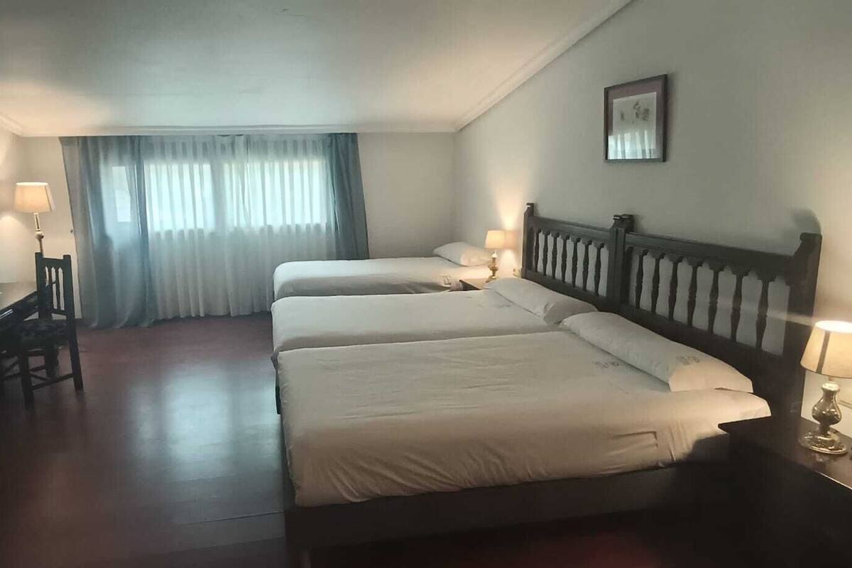 Habitació d'hotel amb dos llits, un escriptori amb cadira, televisió i finestra amb cortines.
