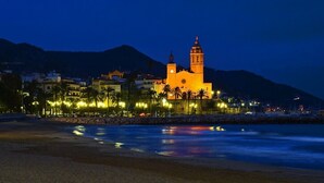 A coastal scene with a prominent church illuminated against a mountain backdrop. - Hotel Celimar (Sitges)