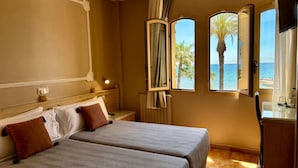A hotel room with two beds, a nightstand, a mirror, and a view of the sea. - Hotel Celimar (Sitges)
