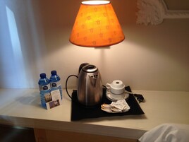 A hotel room's small table with a coffee maker, two water bottles, a tea bag, and a white cup.