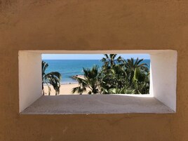 A beach view through a window with palm trees and a clear sky.