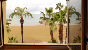 A view from a room with a large window overlooking a beach with palm trees and the ocean. - Hotel Celimar (Sitges)