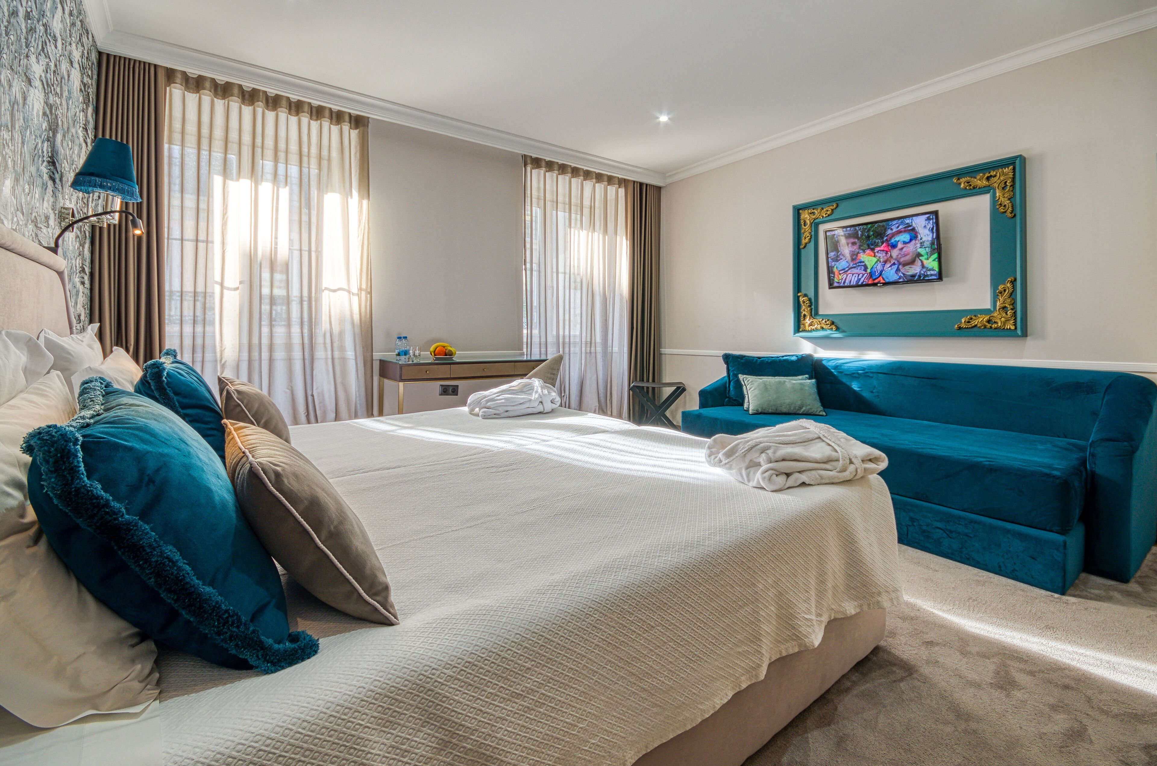 A hotel room with a large bed, a blue sofa, a TV on the wall, and a desk with a lamp.