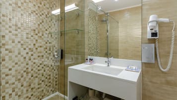 A modern bathroom with a glass shower enclosure, a white sink, and a hairdryer mounted on the wall.