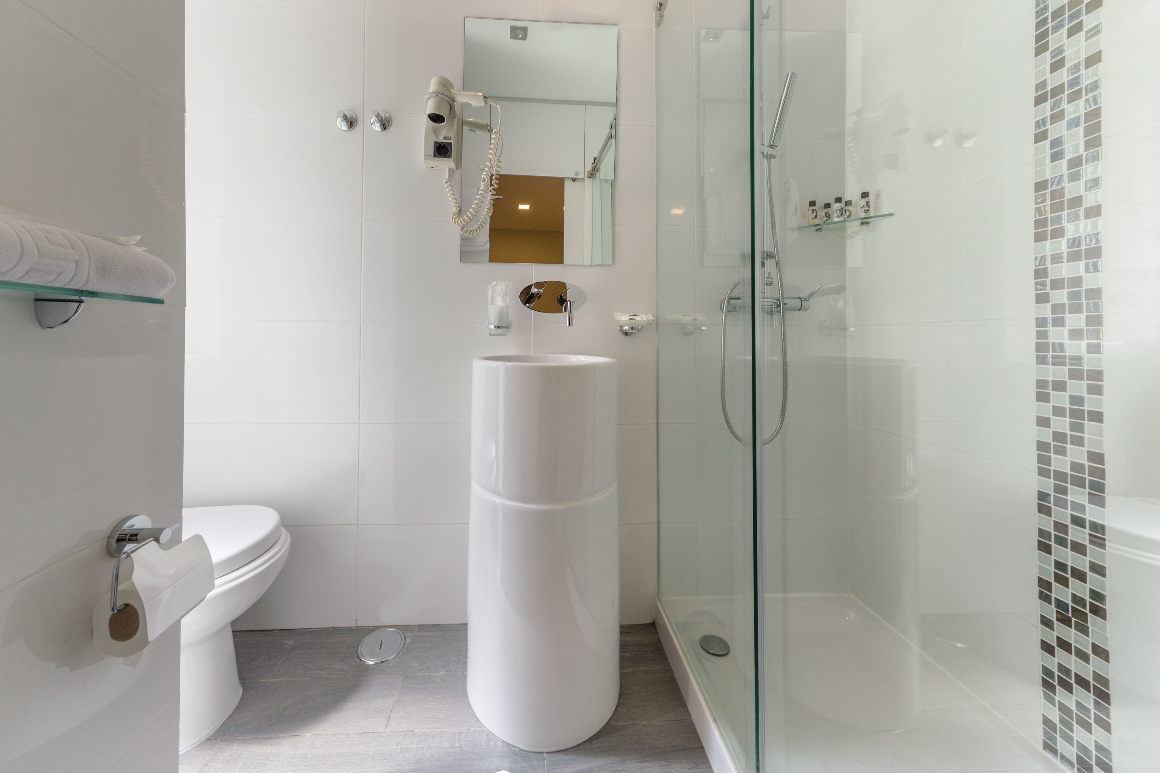 Un baño moderno con inodoro, lavamanos independiente, ducha con mampara de vidrio y espejo sobre el lavamanos.