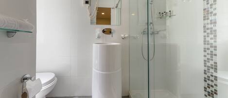 Un baño moderno con inodoro, lavamanos independiente, ducha con mampara de vidrio y espejo sobre el lavamanos.