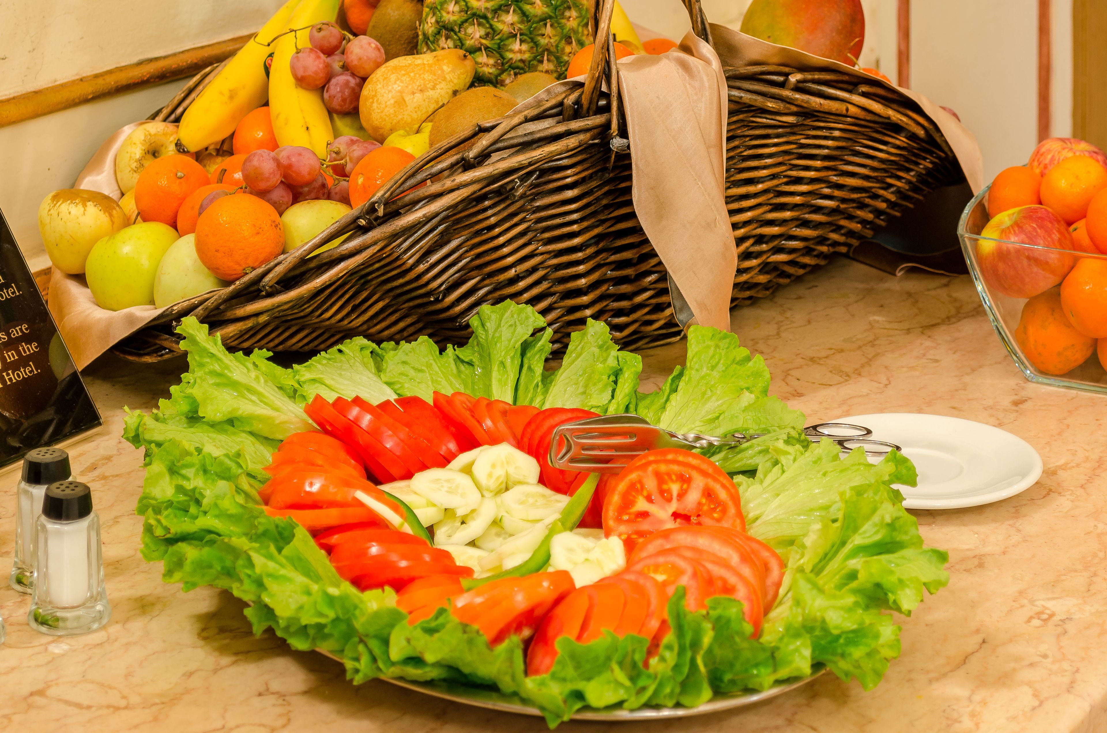 Una cesta de fruta, una ensalada y un bol de naranjas sobre una encimera de mármol.