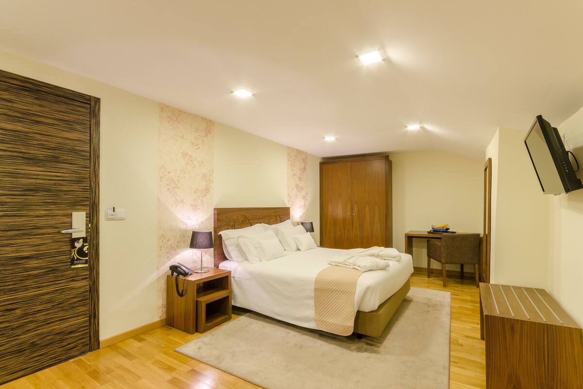 Ein Schlafzimmer mit Bett, Nachttisch, Lampe, Kleiderschrank, Schreibtisch, Stuhl und Fernseher an der Wand.