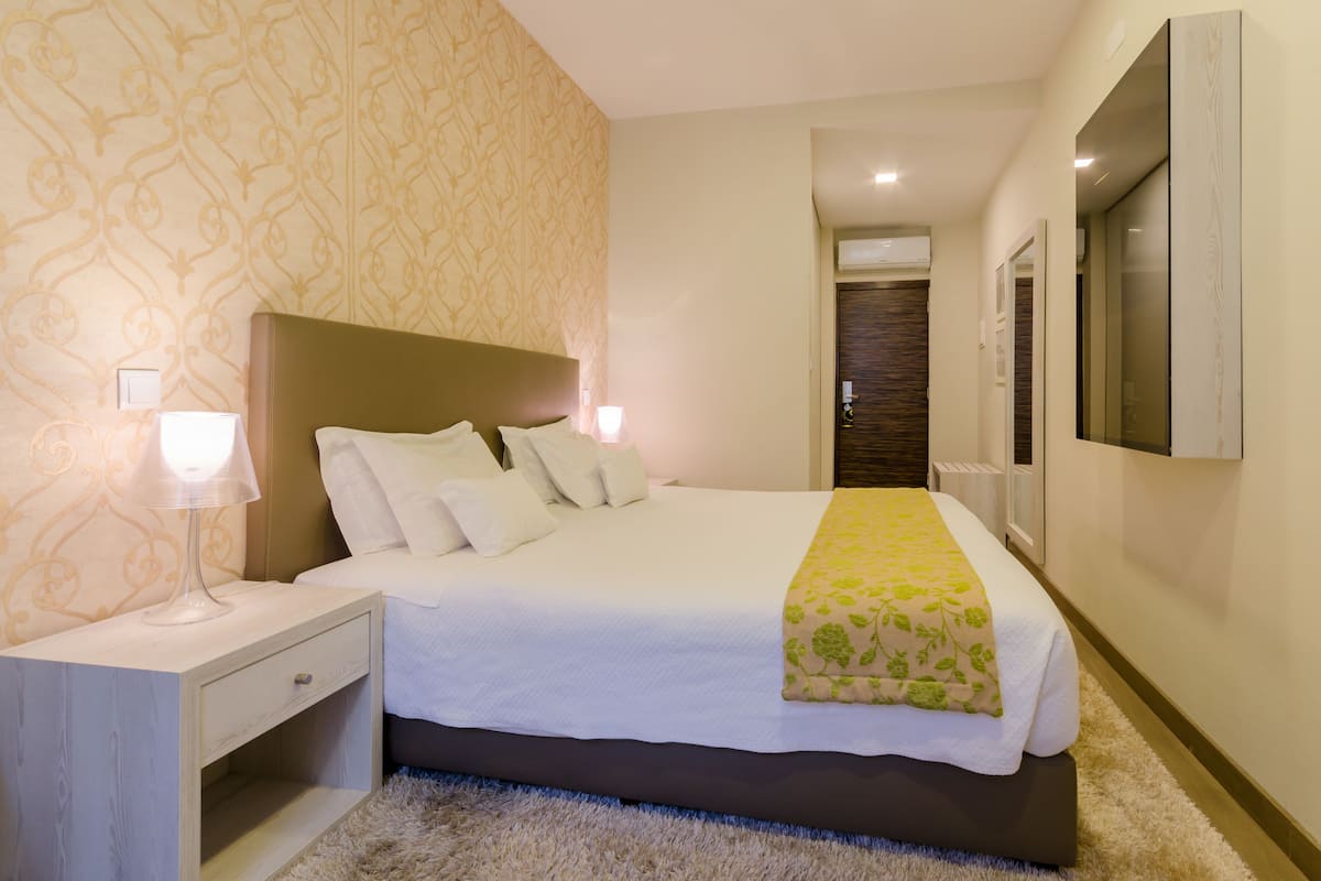 Ein ordentlich eingerichtetes Hotelzimmer mit einem großen Bett, Nachttischlampen, einem Nachttisch und einem an der Wand befestigten Fernseher.