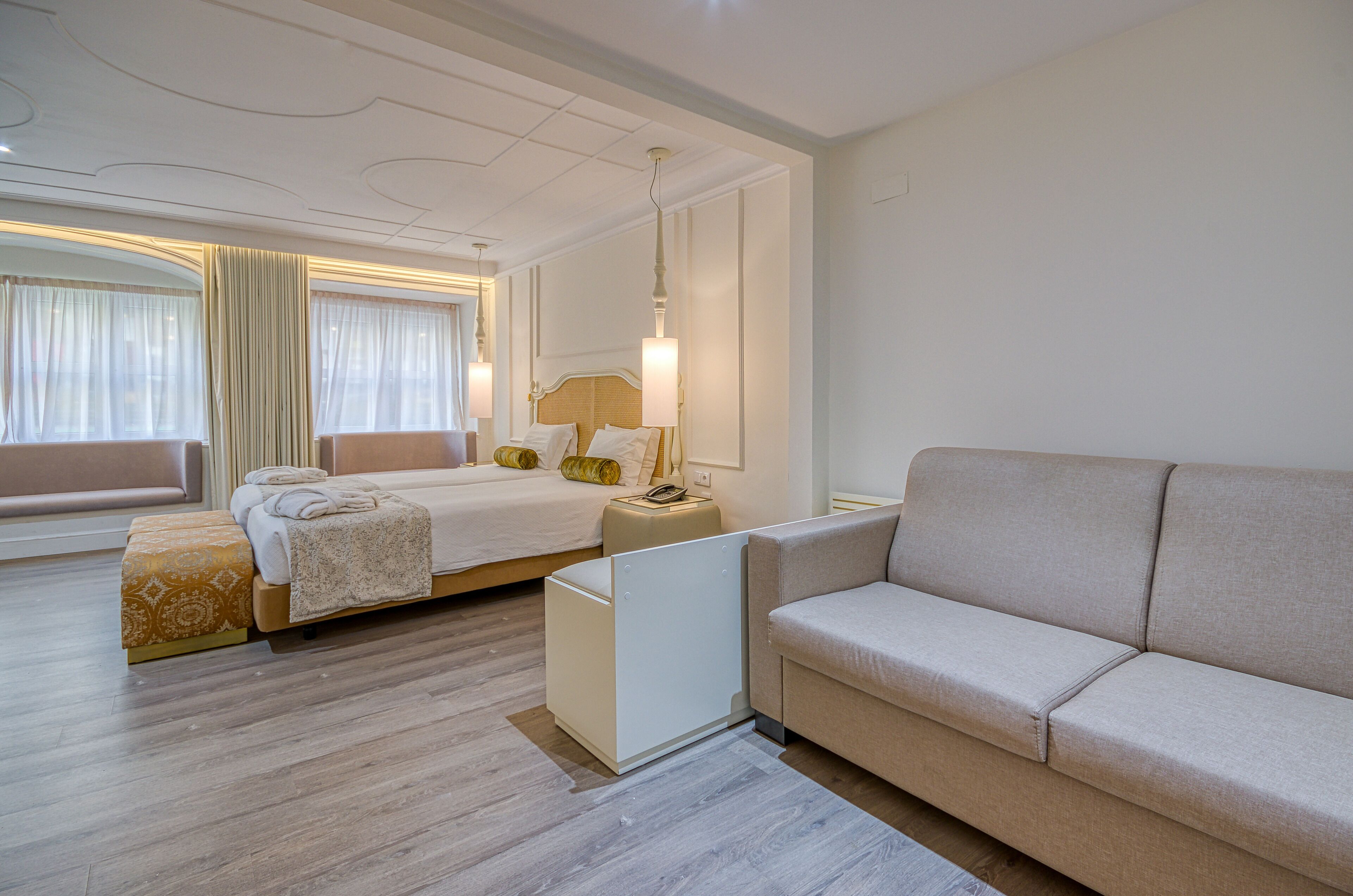 Una habitación de hotel moderna con cama, sofá, mesita de noche y un amplio ventanal con cortinas.