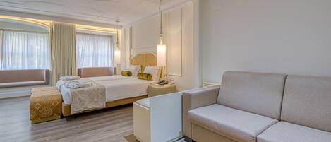 Una habitación de hotel moderna con cama, sofá, mesita de noche y un amplio ventanal con cortinas.