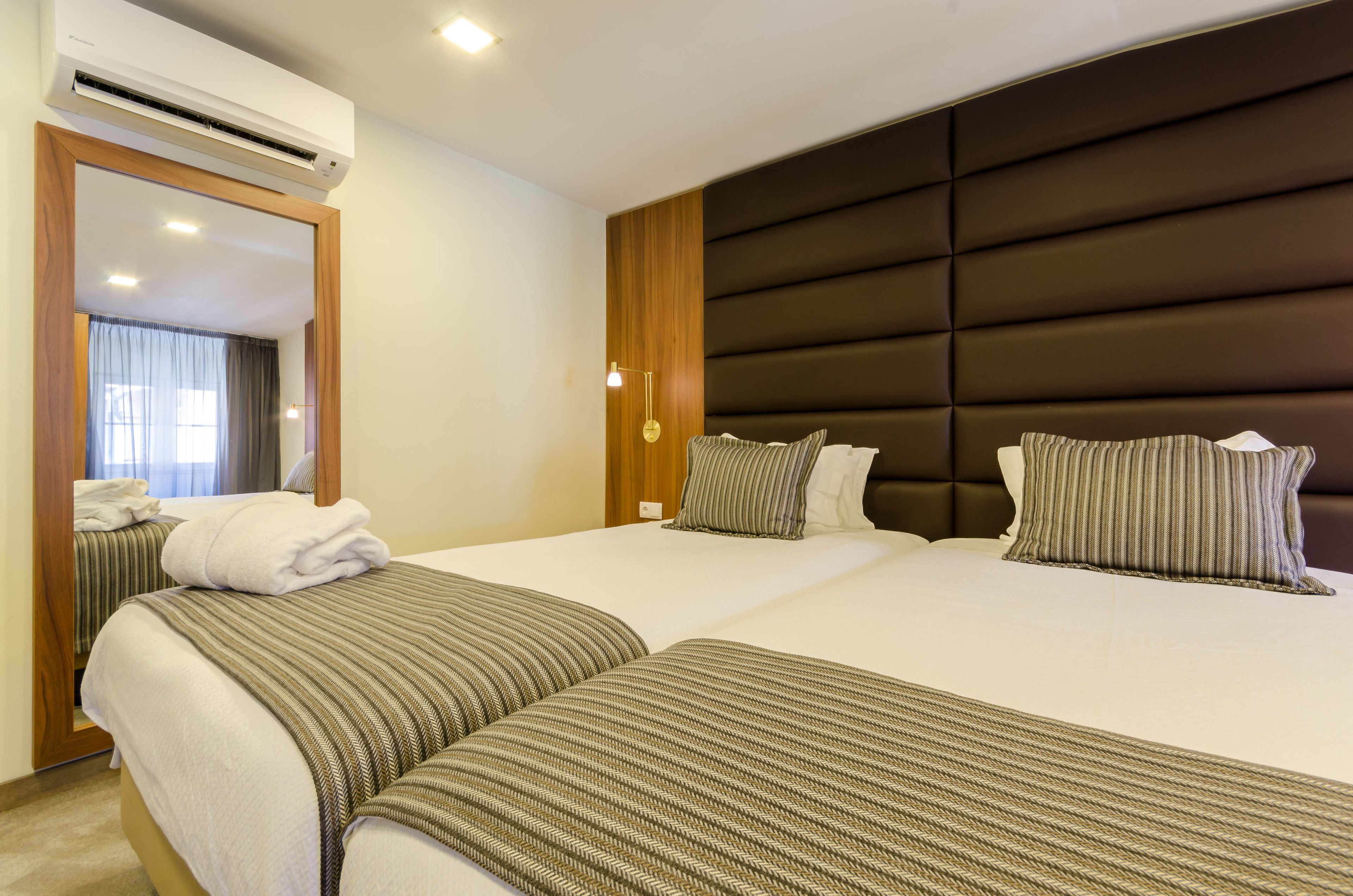 Habitación de hotel con dos camas, un espejo grande y un cabecero moderno.