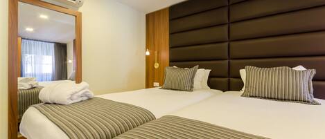 Habitación de hotel con dos camas, un espejo grande y un cabecero moderno.