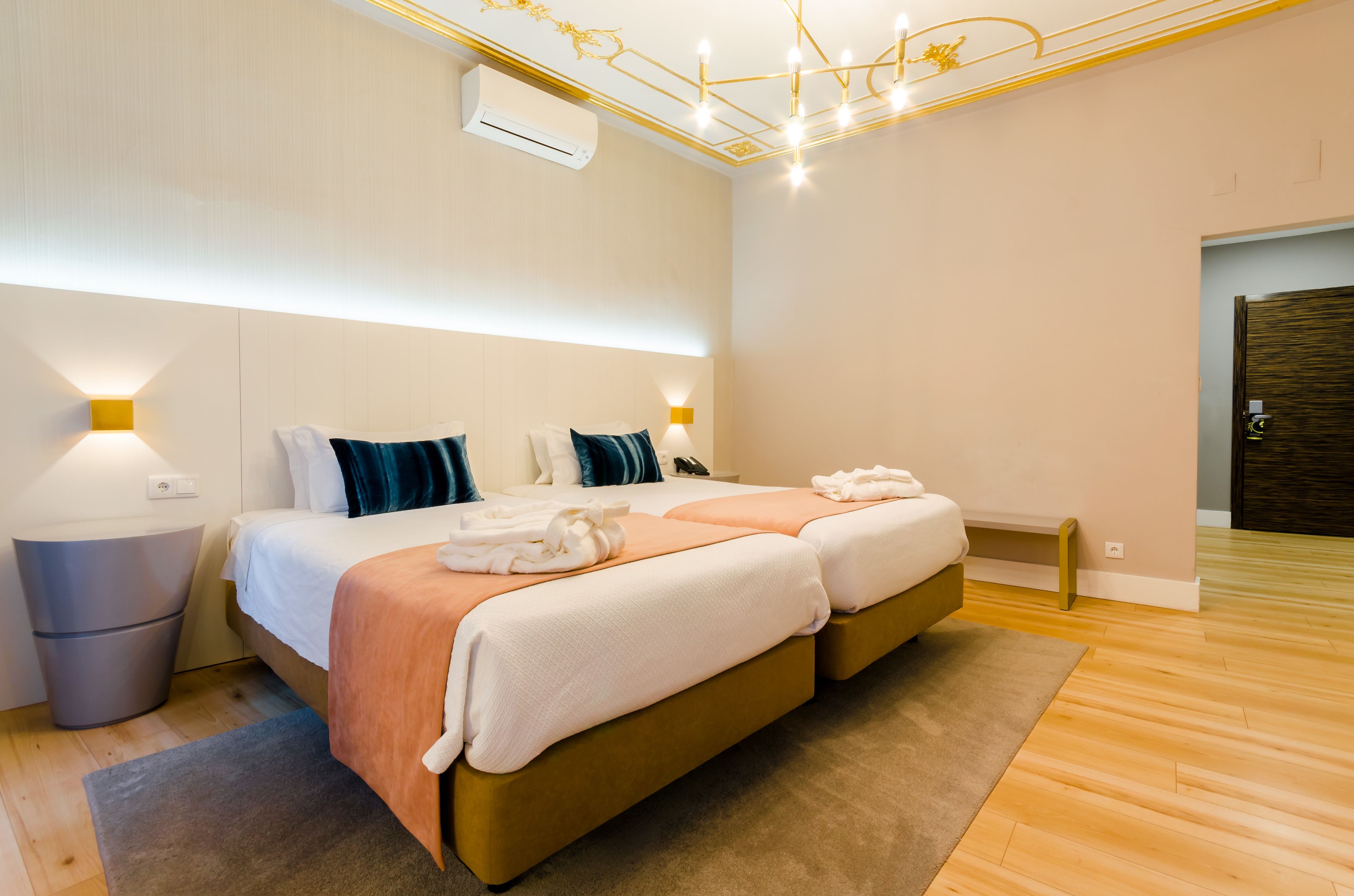A modern hotel room with a double bed, bedside lamps, a small bedside table, and a wooden floor.