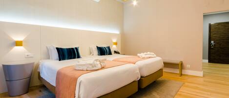 A modern hotel room with a double bed, bedside lamps, a small bedside table, and a wooden floor.