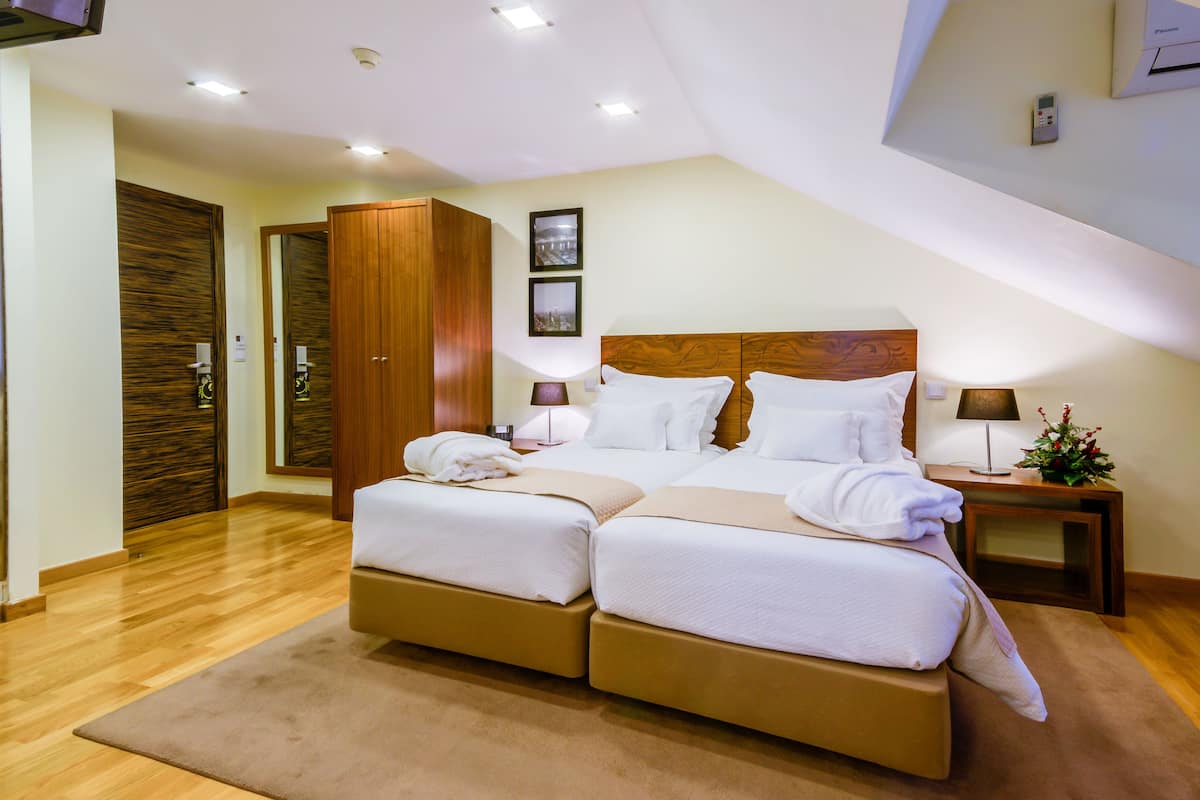 Ein modernes Hotelzimmer mit einem großen Bett, einem Holzschrank und einem kleinen Nachttisch mit Lampe und Blumen.