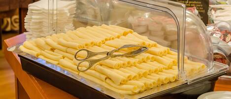 A buffet with a clear glass cover, containing neatly arranged pasta rolls and a pair of scissors on the tray.