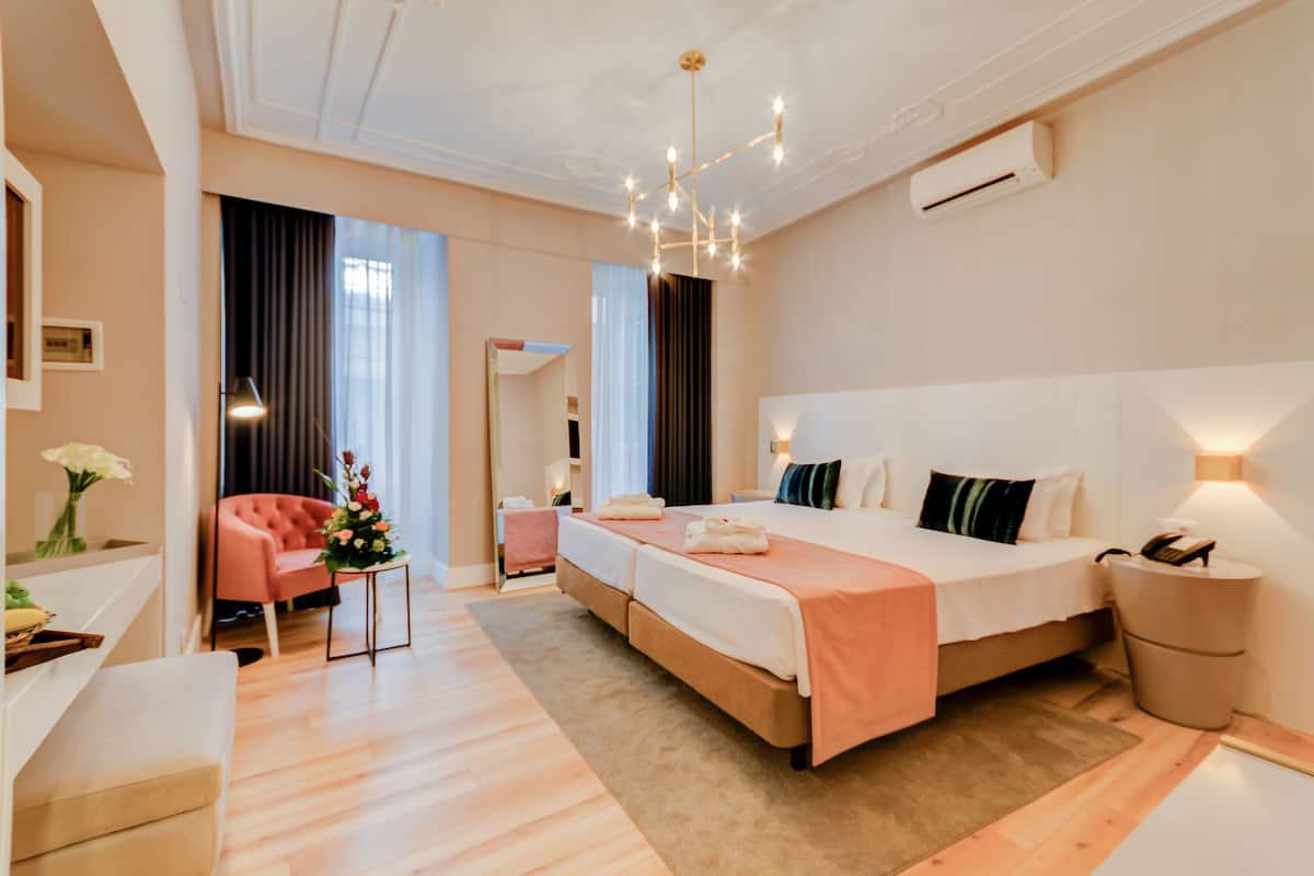 Ein modernes Hotelzimmer mit einem großen Bett, einer Sitzecke mit einem rosafarbenen Sessel, einem kleinen Tisch mit Blumen und einer Nachttischlampe.