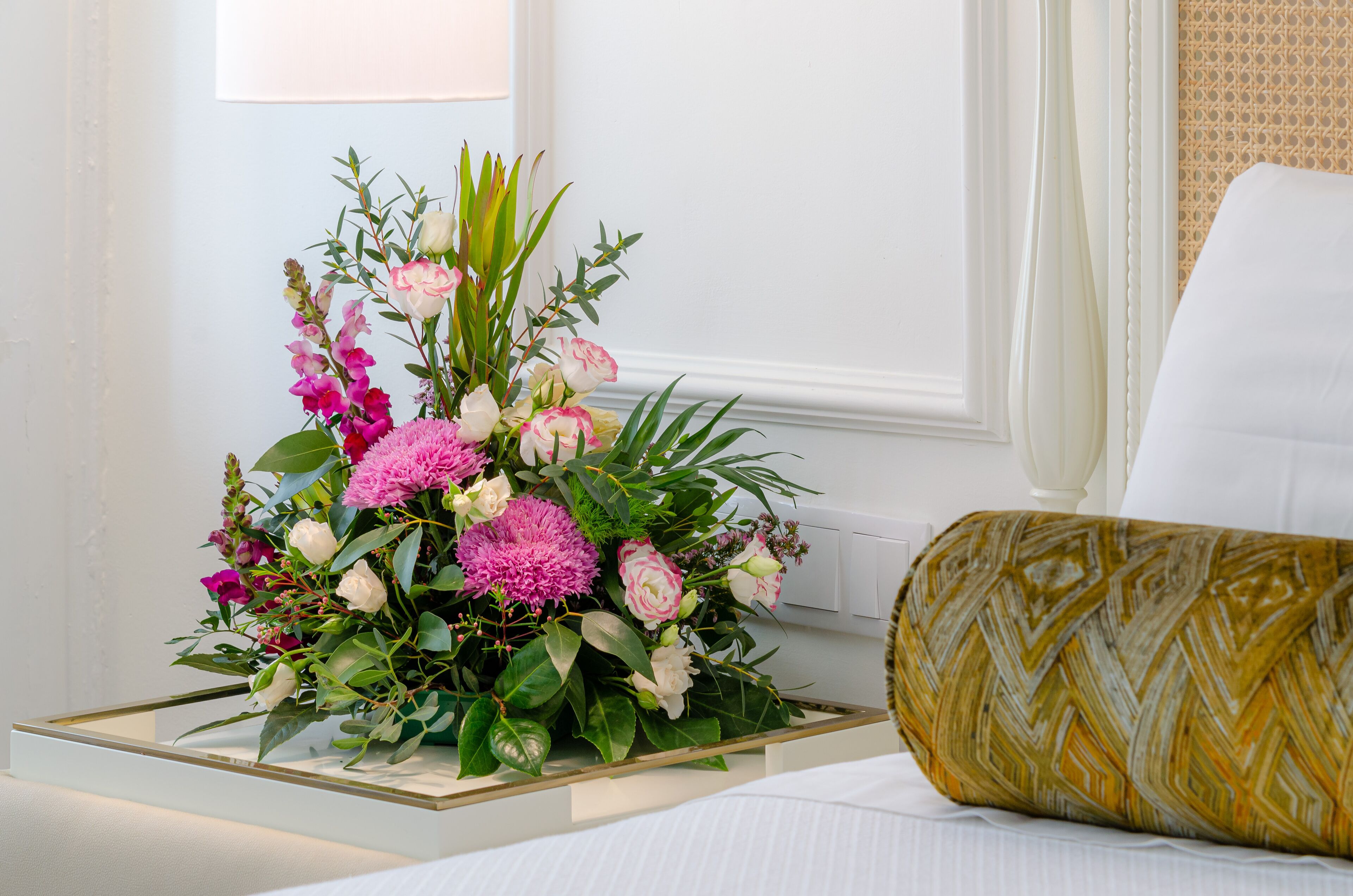 Un letto con un cuscino bianco e un decorativo bouquet di fiori su un comodino.