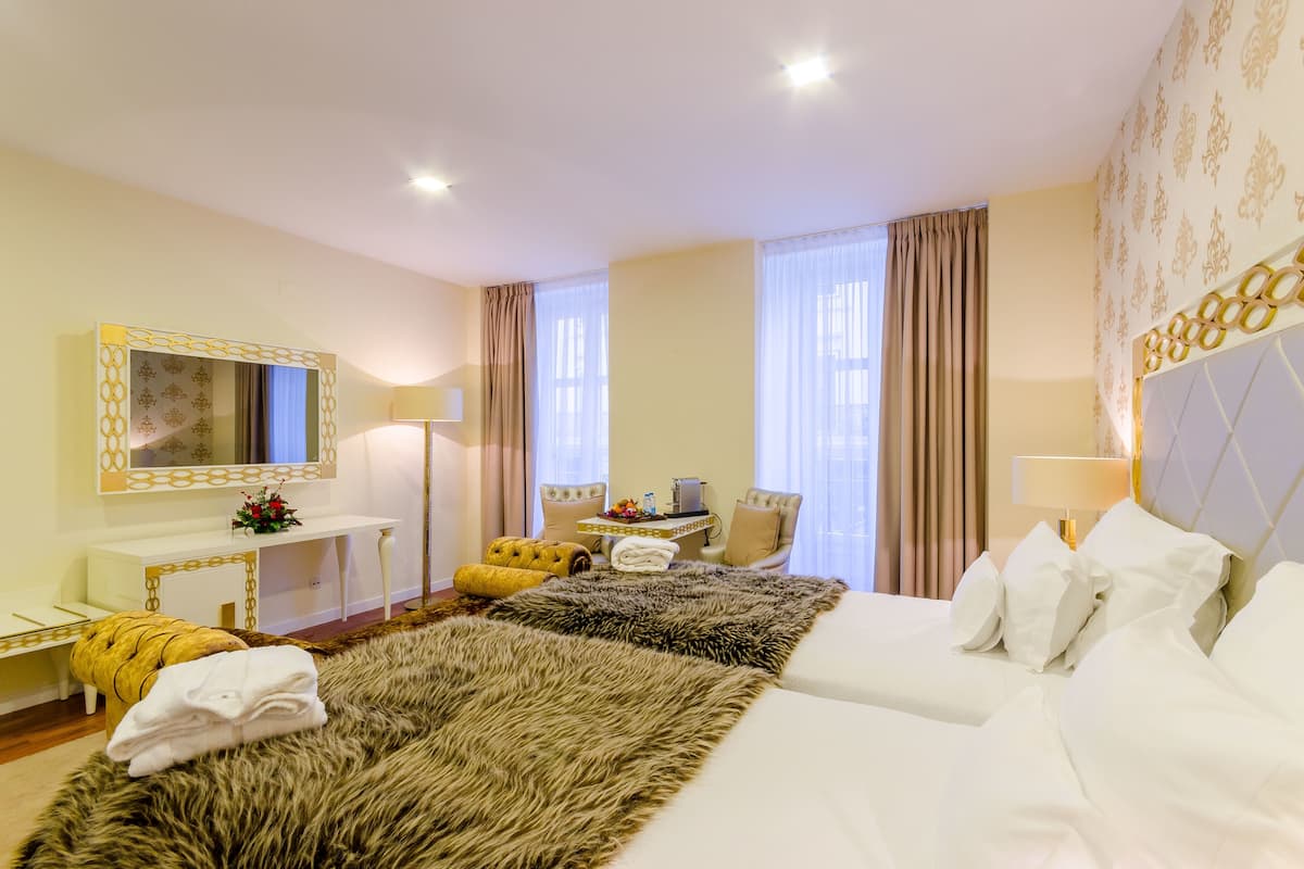 Ein Hotelzimmer mit zwei Betten, einem Schminktisch mit Spiegel, einem Schreibtisch, einem Stuhl und einem großen Fenster mit Vorhängen.