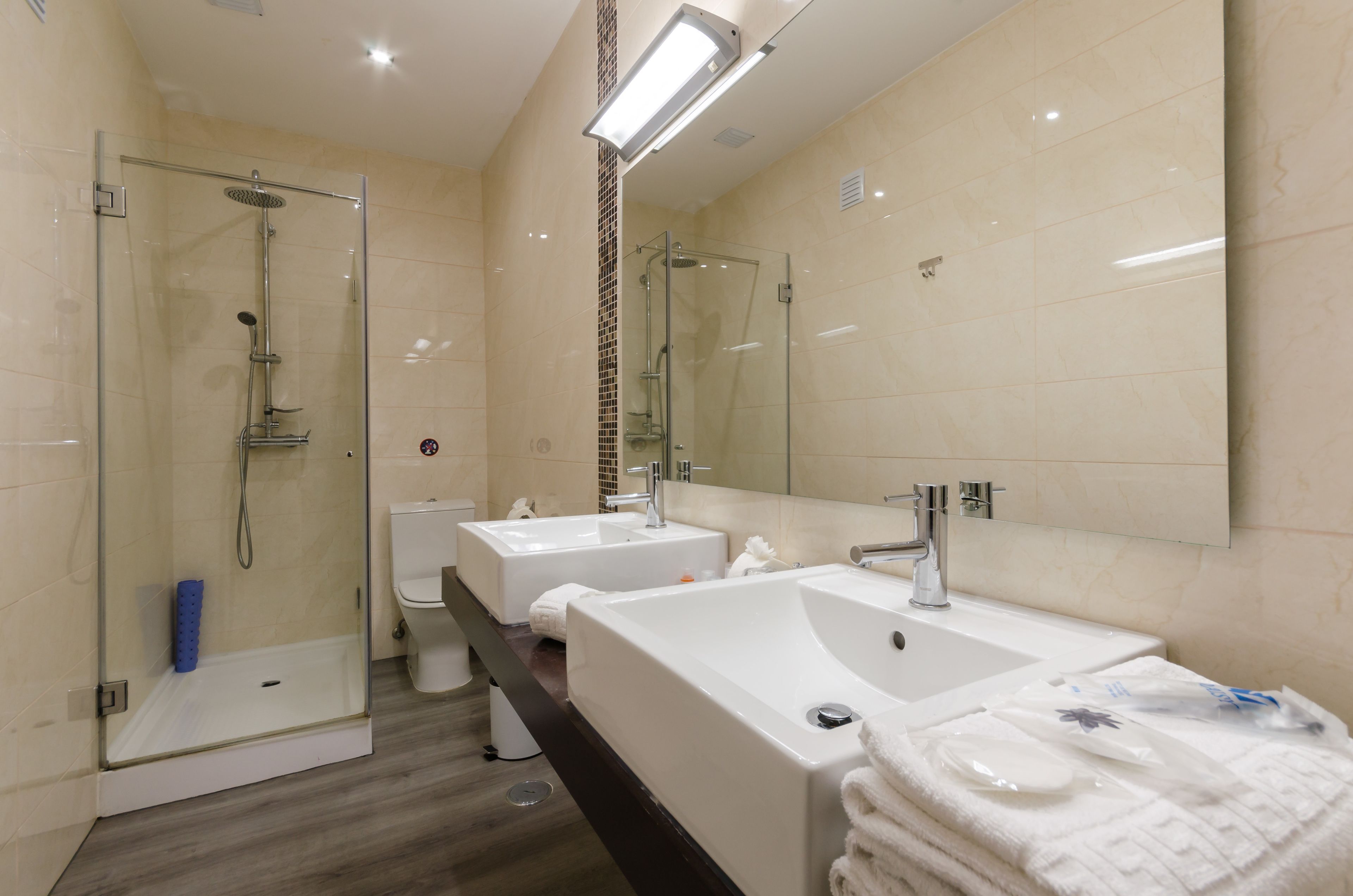 Un bagno moderno con doccia vetro, due lavandini e un ampio specchio.