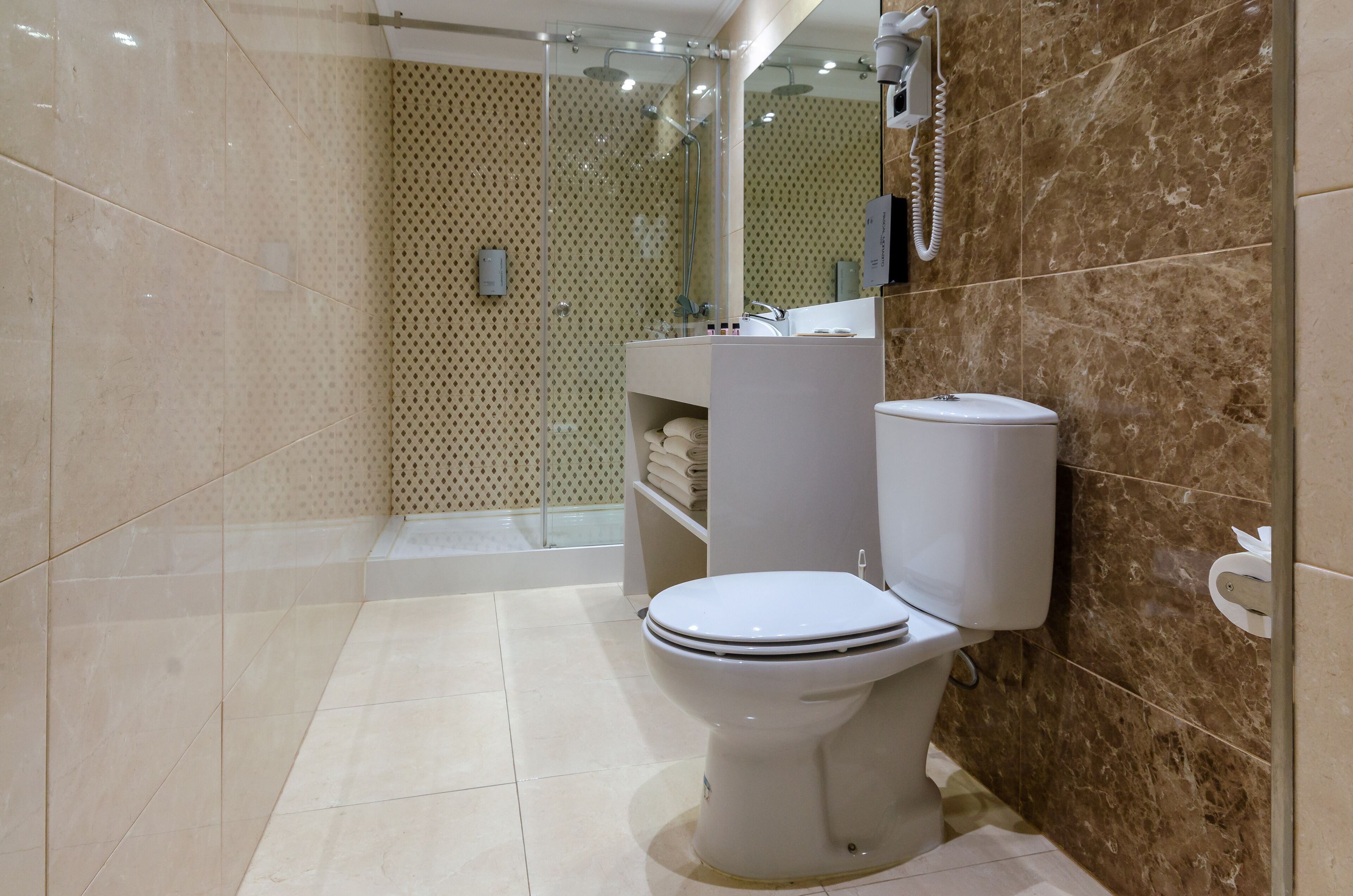 A modern bathroom with a toilet, a glass-enclosed shower, and a marble-tiled wall.