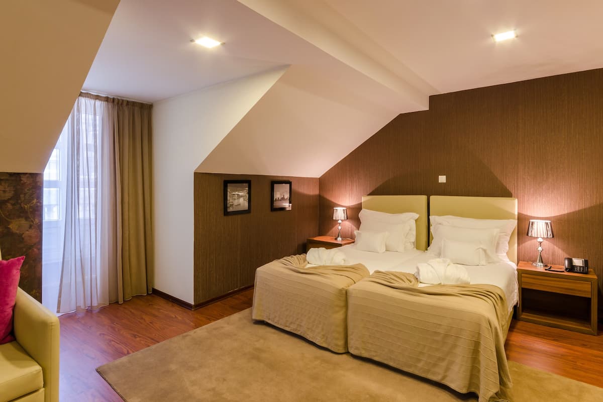 Ein Schlafzimmer mit einem großen Bett, zwei Nachttischen mit Lampen, einem Holzkopfteil, einer Wand mit Steinakzenten und einem Fenster mit Vorhängen.