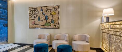 Un hall con tres sillones blancos, un reposapiés azul, una obra de arte de mosaico y un suelo de mármol.
