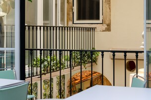 A balcony with a metal railing, a table, chairs, and potted plants.
