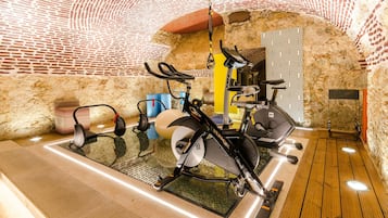 A gym with various exercise equipment, including stationary bikes and treadmills, in a room with stone walls and wooden flooring.