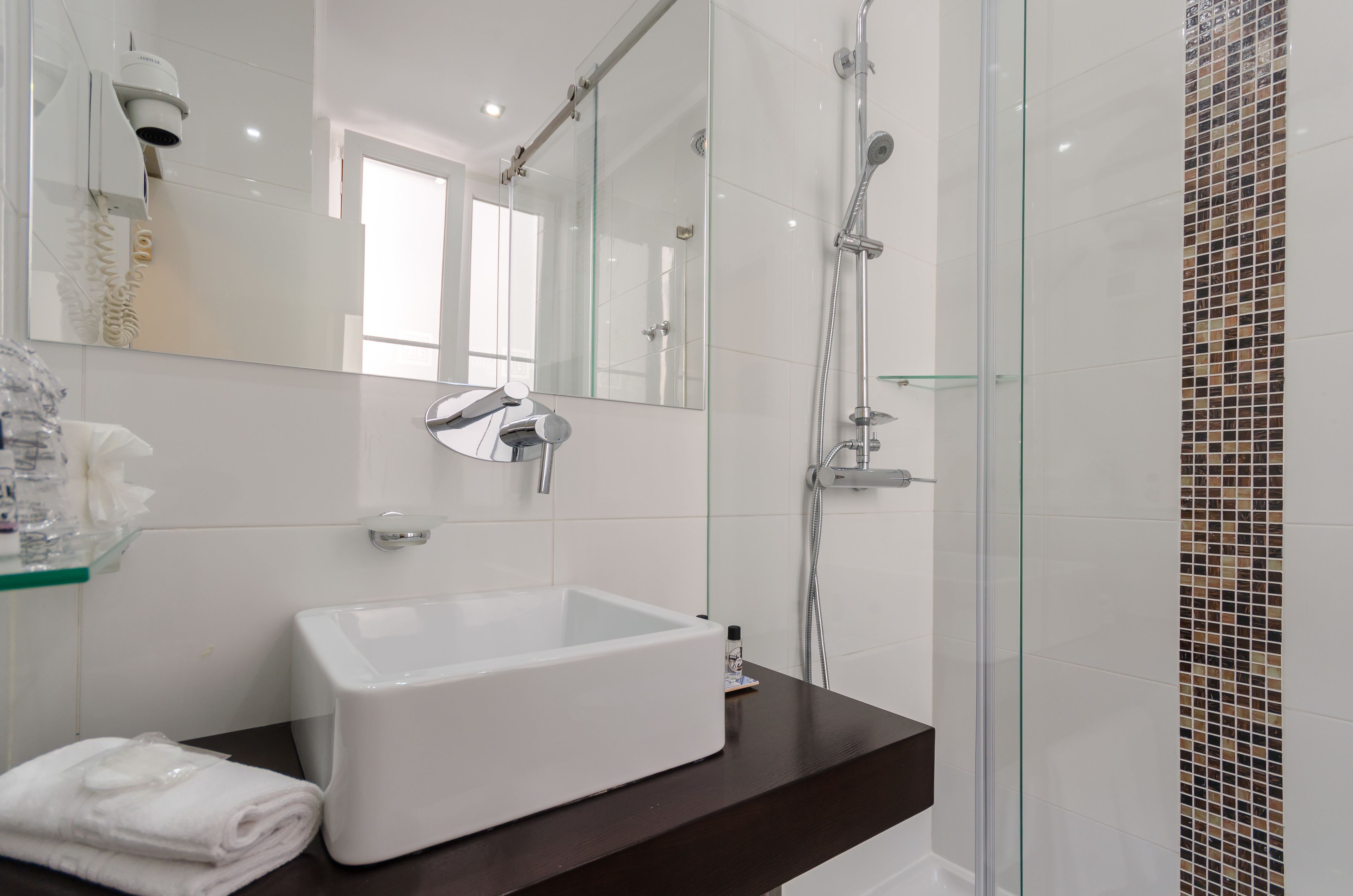 Une salle de bain moderne avec une douche à l’italienne en verre, un lavabo blanc et un grand miroir.