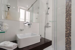 Une salle de bain moderne avec une douche à l’italienne en verre, un lavabo blanc et un grand miroir.
