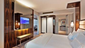 Quarto de hotel moderno com uma cama grande, um banquinho, uma TV e um espelho.