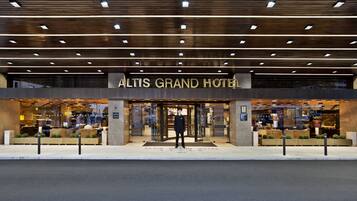 Exterior do Altis Grand Hotel, com design moderno, destacando uma entrada imponente e fachada bem iluminada.