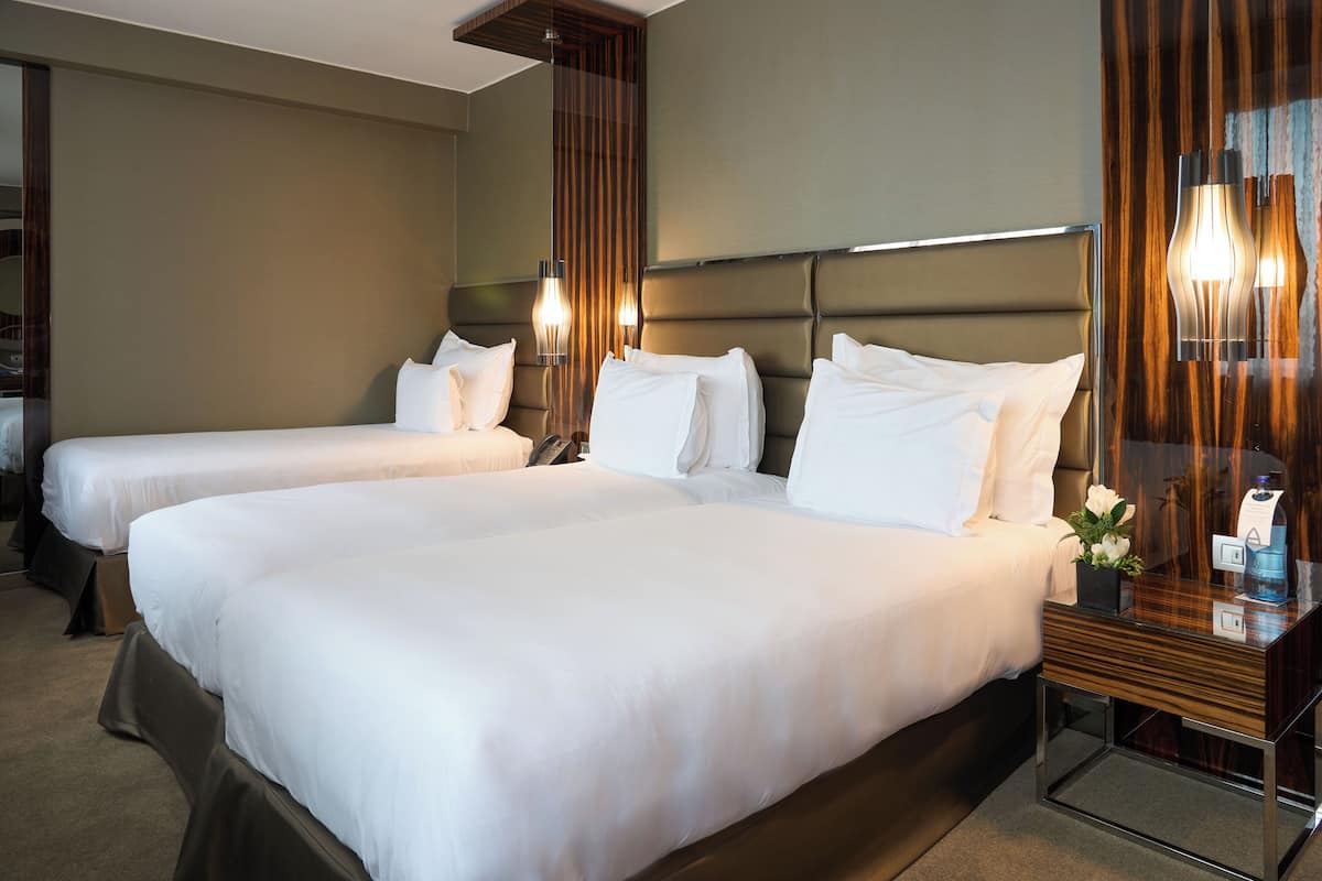 A hotel room with two beds, a wooden headboard, a bedside table with a vase of flowers, and a mirror.