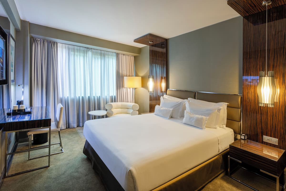 A hotel room with a large bed, a desk, a chair, and a TV.