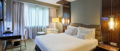 A hotel room with a large bed, a desk, a chair, and a TV.