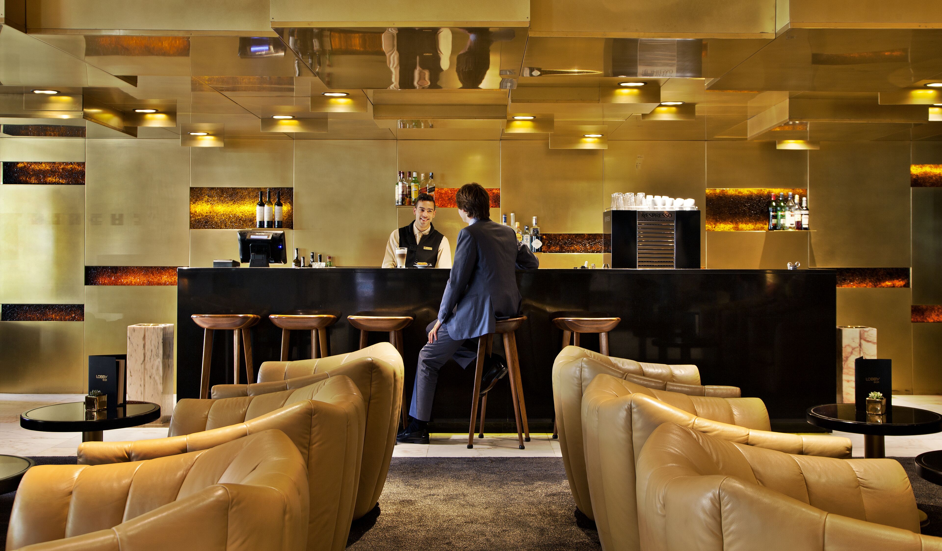 A bar area with leather seating, a counter, and a bartender.