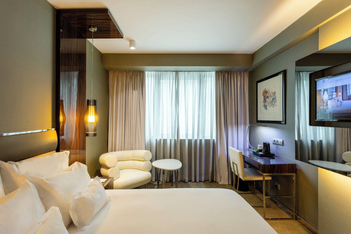 A hotel room with a bed, a desk, a chair, a small table, and a TV.
