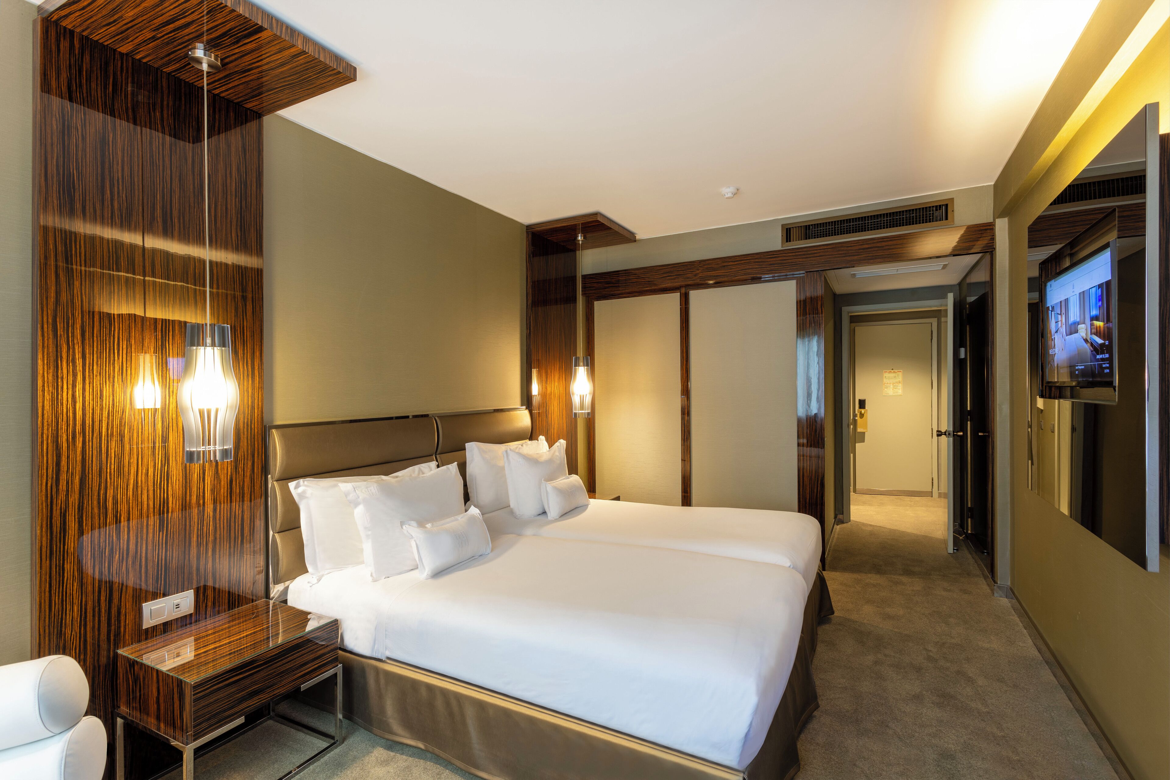 Een moderne hotelkamer met een groot bed, houten lambrisering, een nachtkastje en een televisie.