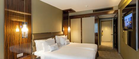 Una habitación de hotel moderna con una cama grande, paneles de madera, una mesita de noche y un televisor.