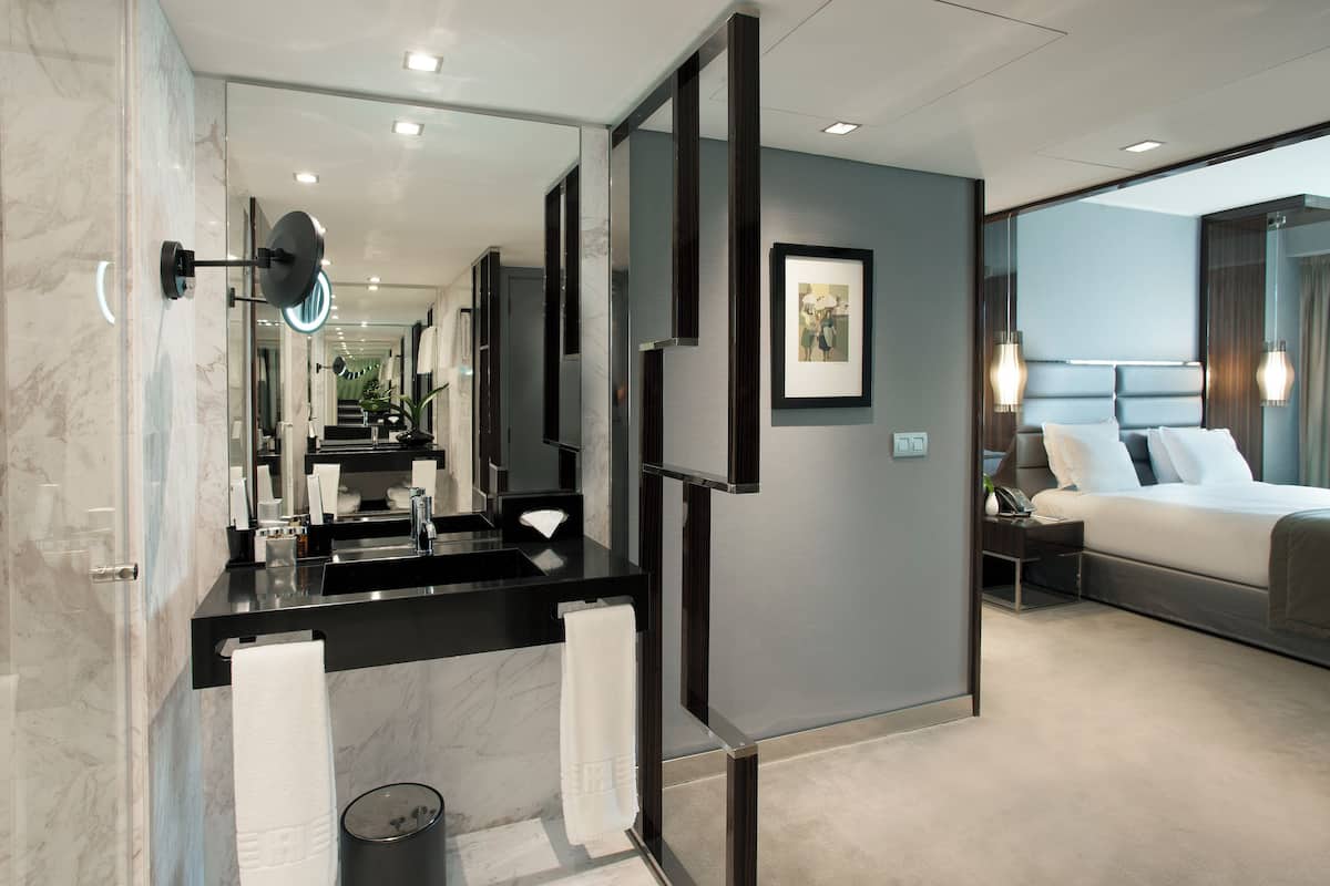 A modern hotel room with a large bed, a separate bathroom with a vanity, and a large mirror.
