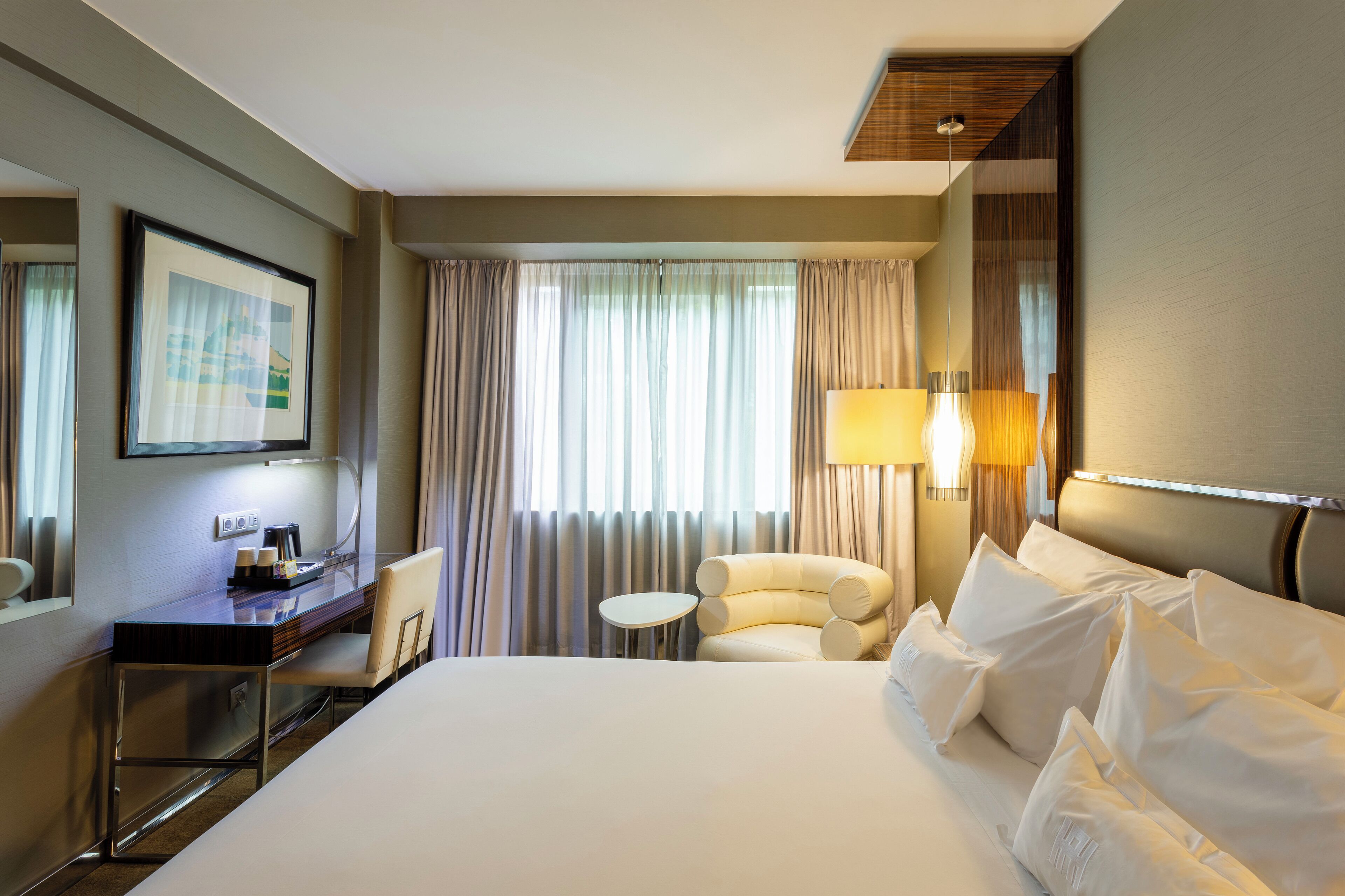 Habitación de hotel con una cama grande, un escritorio con silla, una mesita redonda y una lámpara.