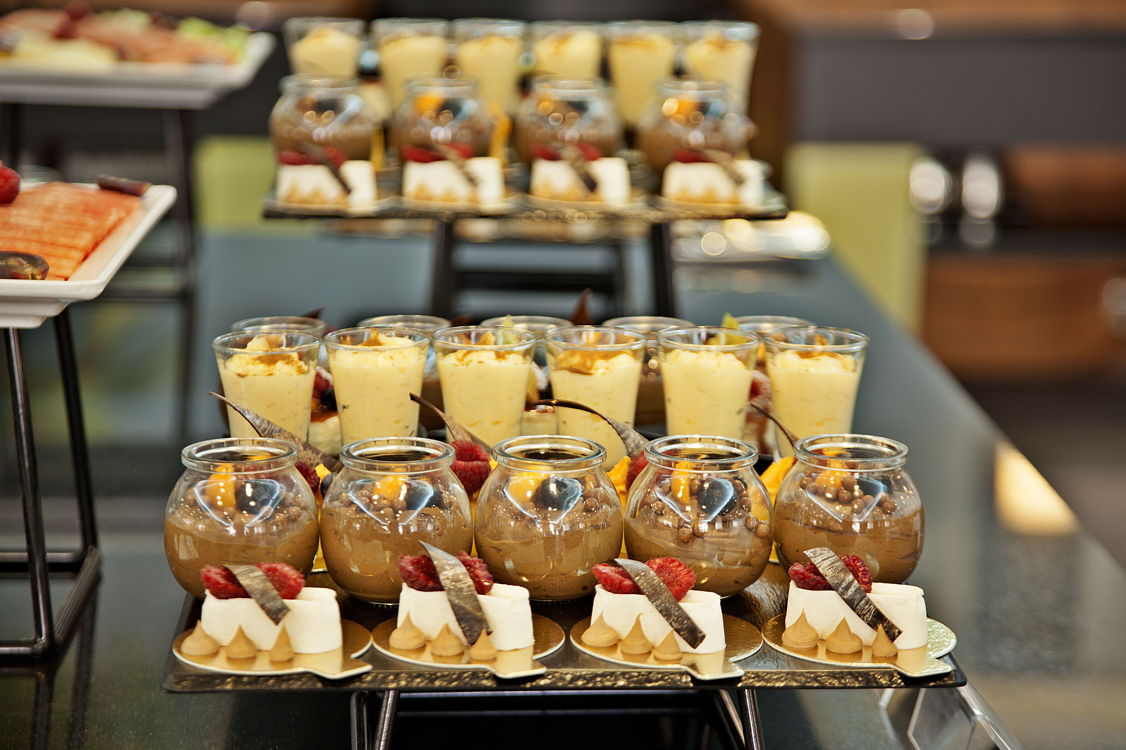 Una mesa de buffet con diversos postres y bebidas, incluyendo botes de mousse de chocolate y vasos de ponche de frutas.