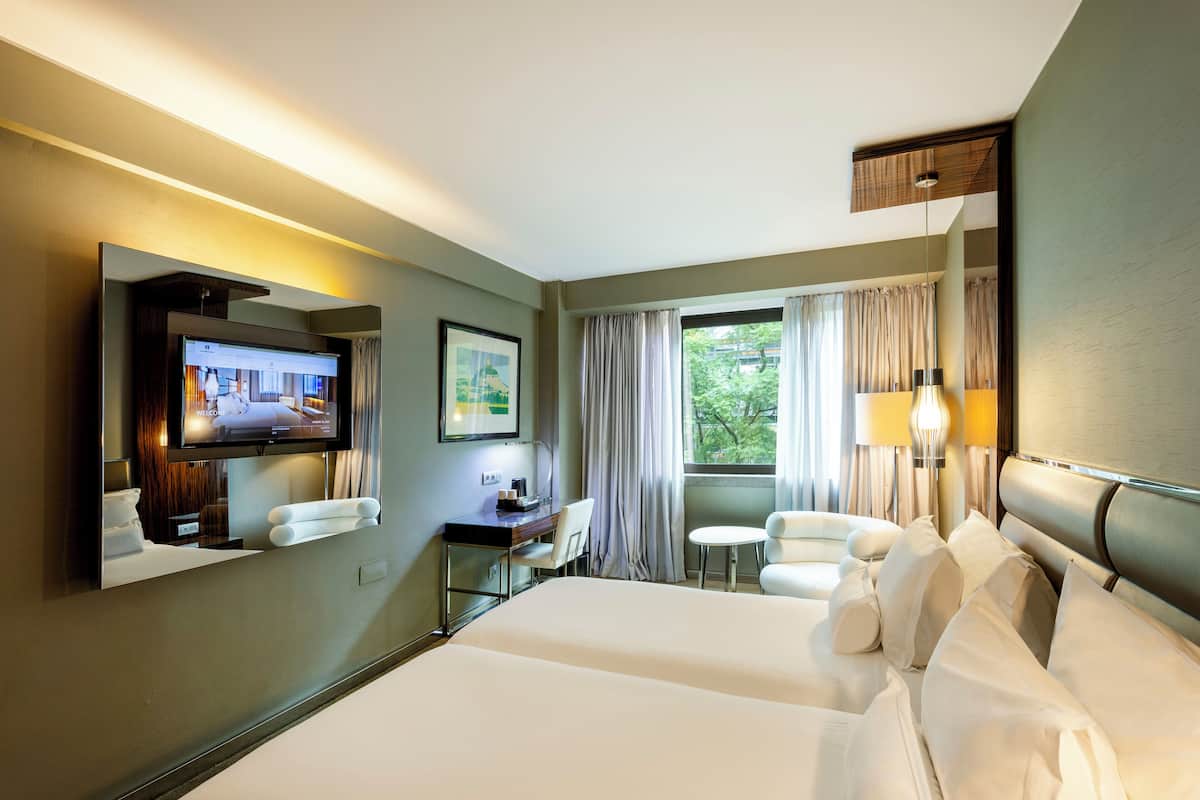 A hotel room with a large bed, a desk with a chair, a television, and a window with curtains.