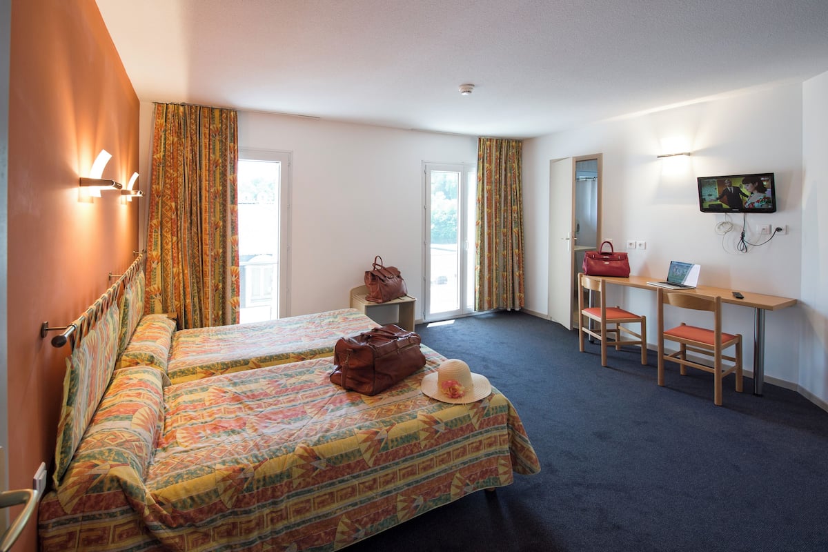 A hotel room with two beds, a desk, a chair, a TV, and a window.